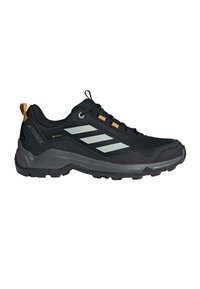 Zapato de senderismo negro con parte superior de malla texturizada, franjas reflectantes y acentos naranjas. Cuenta con una suela resistente para agarre y soporte.