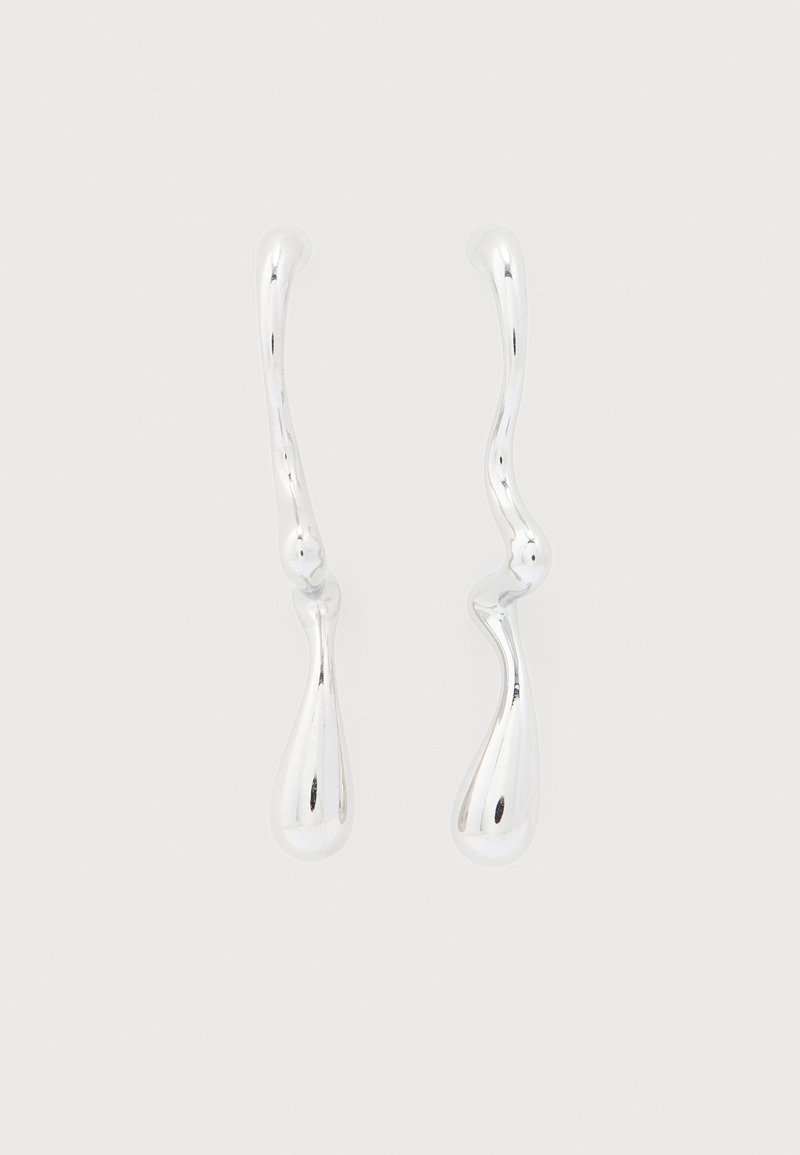 Δύο ακανόνιστου σχήματος σκουλαρίκια σε σχήμα σταγόνας, γυαλιστερά ασημί, με καμπυλωτά στελέχη, πάνω σε απλό λευκό φόντο.