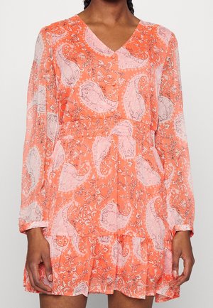 Femme portant une mini-robe à manches longues orange avec un imprimé paisley et floral rose, un col en V, une taille cintrée et un ourlet à volants.