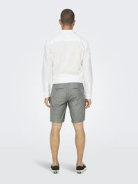 Chemise blanche à manches longues, short gris et chaussures noires à enfiler. La chemise présente un col avec des poignets à boutons, et le short est de longueur genou.