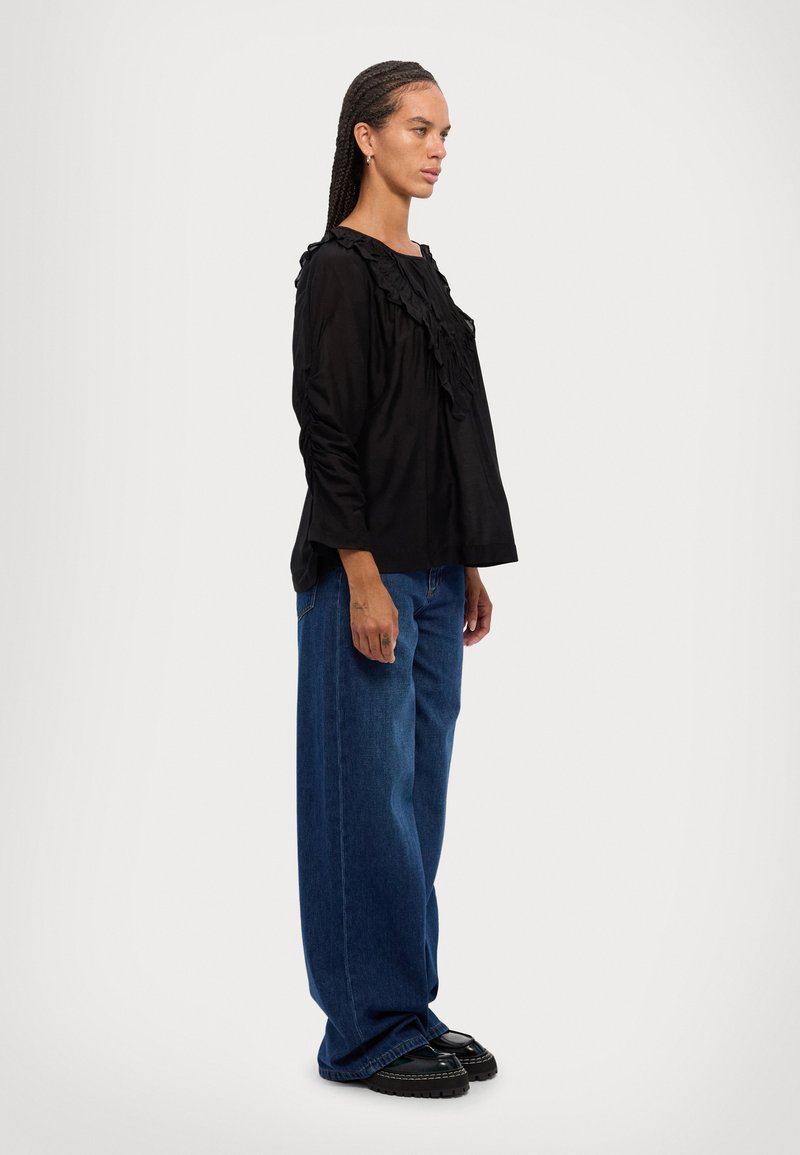 Black long-sleeve top with ruffled neckline, paired with loose blue denim jeans and black platform shoes. The outfit has a relaxed fit.