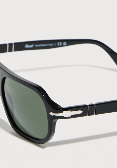 Μαύρα ορθογώνια γυαλιά ηλίου με πράσινους φακούς και ασημένια διακόσμηση σε σχήμα βέλους στα πλαινά σκέλη.