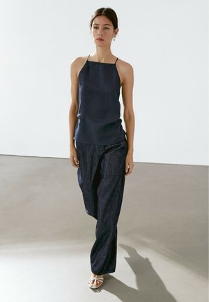 Navy blue, sleeveless top with thin straps, paired with matching wide-legged pants. Smooth texture with subtle sheen. White open-toe shoes.