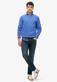 Sudadera de algodón azul claro con cuello redondo, combinada con jeans de mezclilla oscura. Los accesorios incluyen un cinturón marrón y zapatillas blancas con detalles en negro.