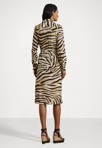 Abito a maniche lunghe con motivo a zebra in beige e marrone, caratterizzato da un colletto, vita con cintura e lunghezza midi, abbinato a sandali neri con plateau.