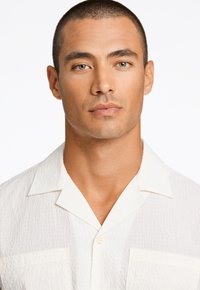 Witte, gestructureerde short-sleeve blouse met een kraag en knopen, voorzien van een patch pocket en een subtiele, gekreukte stofpatroon.