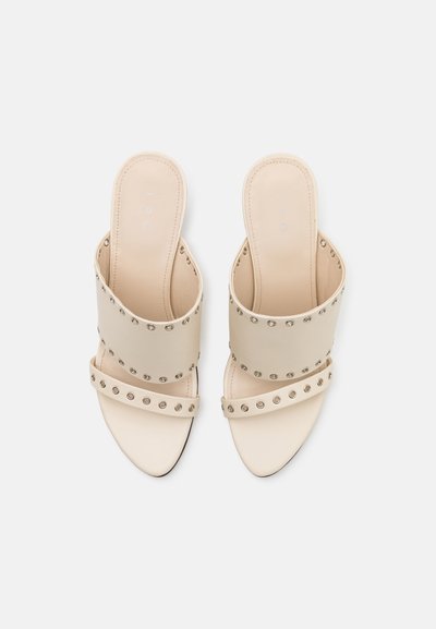 Beige slippersandalen met brede bandjes, versierd met zilveren studs, met een gevoerd voetbed en een elegante puntige teenvorm.