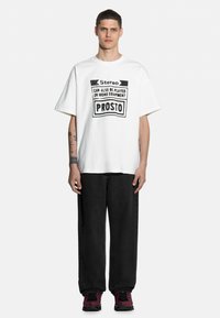Biała bawełniana koszulka z czarnym nadrukiem graficznym z napisem "Stereo Can Also Be Played On Mono Equipment PROSTO." Luźny krój, krótkie rękawy.