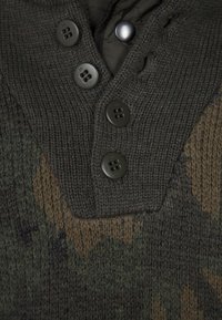 Gestrickter Pullover mit Tarnmuster in Dunkelgrün und Braun, mit V-Ausschnitt, drei schwarzen Knöpfen und charakteristischer strukturierter Stoff.