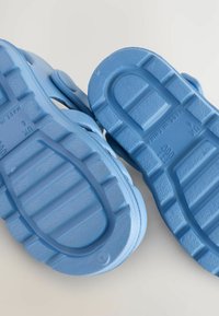 Blå gummisandaler med texturerade sålar, som har ett brett rem och ett mönster av räfflor. Storlek 6 markerad på undersidan.