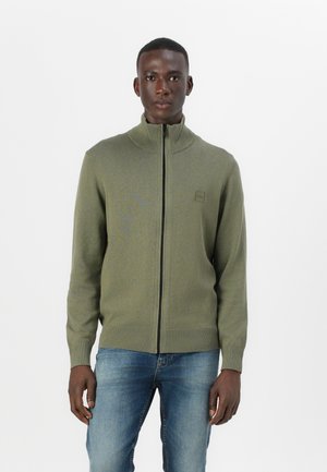 Olive green zip-up sweater with a high collar, ribbed cuffs, and hem. Features a small logo on the chest, made from a soft knit material.