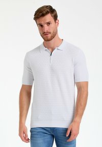 Polo de manga corta en gris claro con un patrón de diamantes texturizado, que presenta un cierre de media cremallera en el frente y un detalle de cuello en contraste.