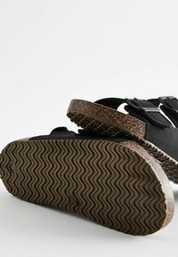 Svarta sandaler med korksoffa, med två justerbara remmar och en texturerad gummisula. Fotbädden är vadderad för komfort.