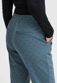 Blaue Polka-Dot-Hosen mit einer lockeren Passform, elastischem Bund und Seitentaschen, aus glattem Stoff mit einer leicht strukturierten Oberfläche.