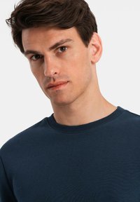Sudadera de cuello redondo en azul marino hecha de tejido suave; cuenta con un cuello acanalado y una textura lisa sin patrones ni acentos visibles.