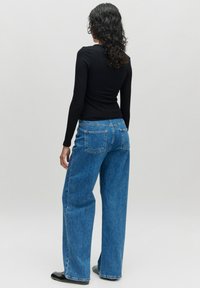 Blaue Denim-Jeans mit lockerer Passform, hoher Taille und Gesäßtaschen. Dazu ein schwarzes Langarmshirt. Rückansicht dargestellt.