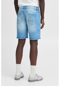 Shorts en denim bleu clair avec une coupe droite, dotés d'ourlets effilochés et de deux poches arrière. Portés avec des baskets grises et des chaussettes blanches.