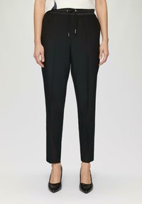 Zwarte broek met een elastische tailleband en trekkoord, met een gladde textuur, taps toelopende pijpen en een getailleerde pasvorm.