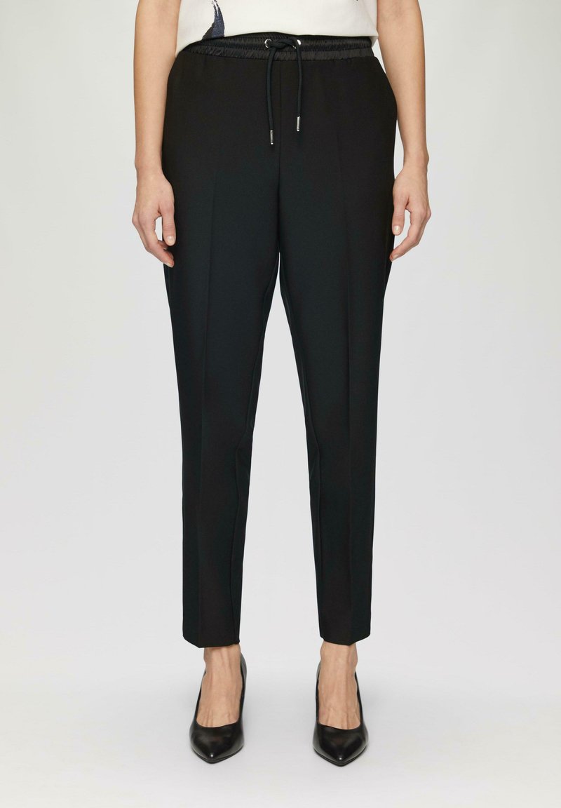 Zwarte broek met een elastische tailleband en trekkoord, met een gladde textuur, taps toelopende pijpen en een getailleerde pasvorm.