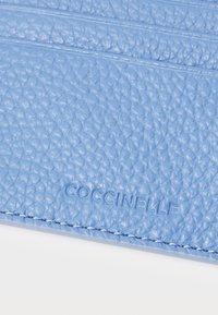 Portafoglio in pelle texturizzata azzurro chiaro con logo "COCCINELLE" impresso, cuciture sottili e più scomparti per carte per una migliore organizzazione.