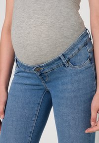 Trenirka za nosečnice v svetlo modrem jeansu, s prožnim pasom in sprednjimi žepi. Gladek tekstura s priložnostnim krojem.