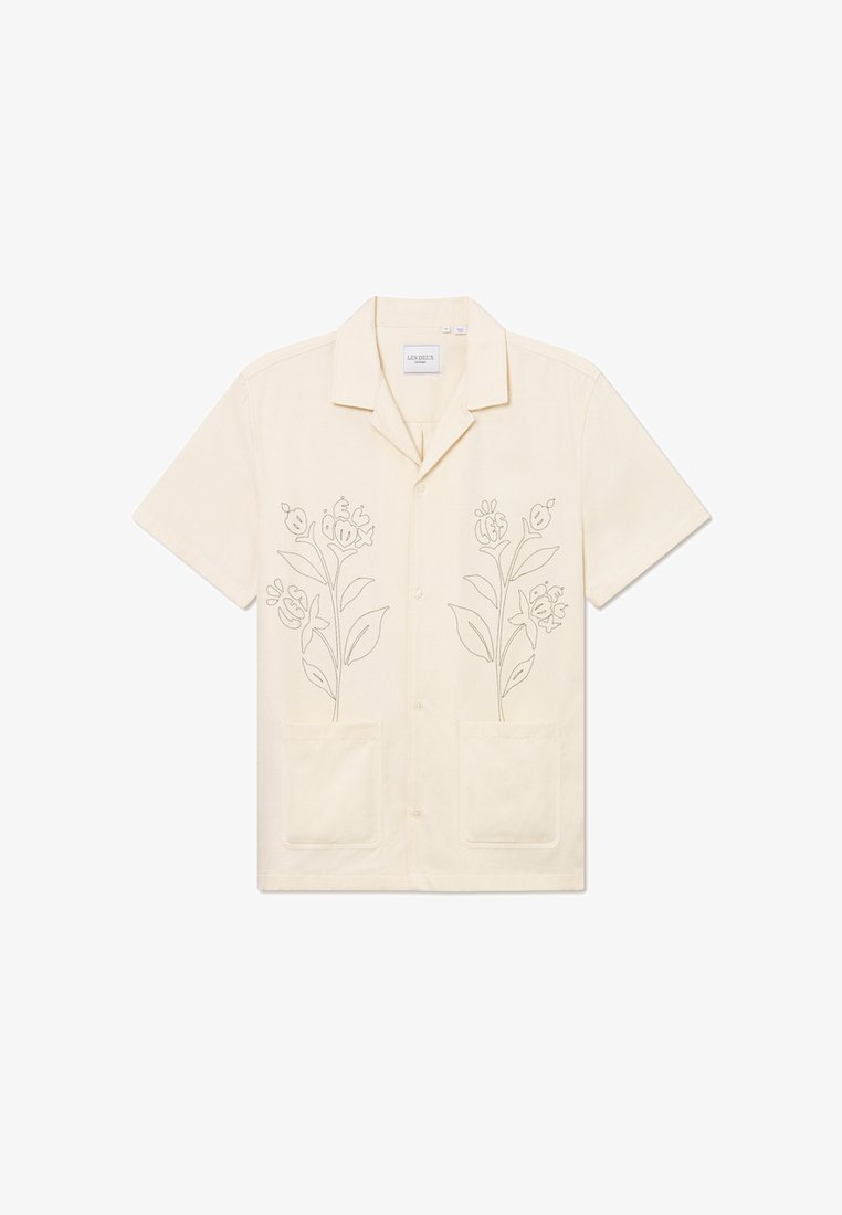 Trumpas rankovės, šviesiai krėminis marškinis su mygtukais ir gėlių siuvinėjimu priekyje. Turi dvi priekinės kišenes ir klasikinio apykaklės dizainą.