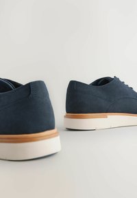 Scarpe in suede blu navy con pannello in rete, punta rotonda e suola in gomma tan. Presentano dettagli cuciti e design con lacci.