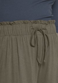 Olive green pants with elastic waistband, gathered top, and drawstring detail, paired with a ribbed navy top.