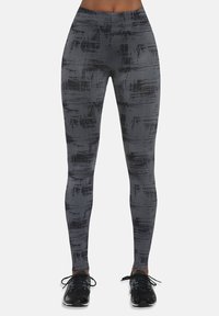 Szare legginsy z fakturowanym, abstrakcyjnym czarnym wzorem, wysokim stanem i elastycznym materiałem, w zestawieniu z czarnymi butami sportowymi.