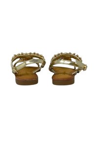 Sandali color oro con suola piatta, caratterizzati da più cinturini e decorazioni in perline, realizzati in materiali sintetici.