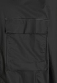 Black jacket featuring a large, square pocket on the left side, crafted from smooth, water-resistant material with stitched edges.