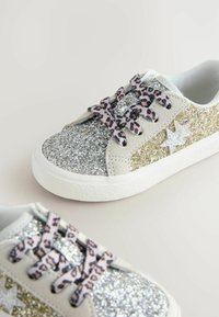 Zapatillas con glitter en una mezcla de brillantes plateados y dorados, acentos de ante beige y cordones de estampado de leopardo. Cuentan con suelas de goma blanca.