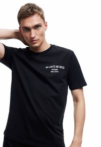 Camiseta negra de algodón con cuello redondo, mangas cortas y texto impreso en blanco en el frente que dice "SIN LÍMITES SIN REGLAS".