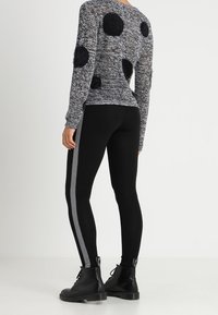 Pull texturé noir et blanc avec des pois noirs duveteux, associé à des leggings noirs ajustés avec une bande blanche, et des bottines noires.