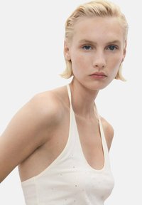 Top a halter color crema con spalline sottili, caratterizzato da sottili accenti luccicanti. Tessuto morbido e vestibilità comoda messi in risalto.