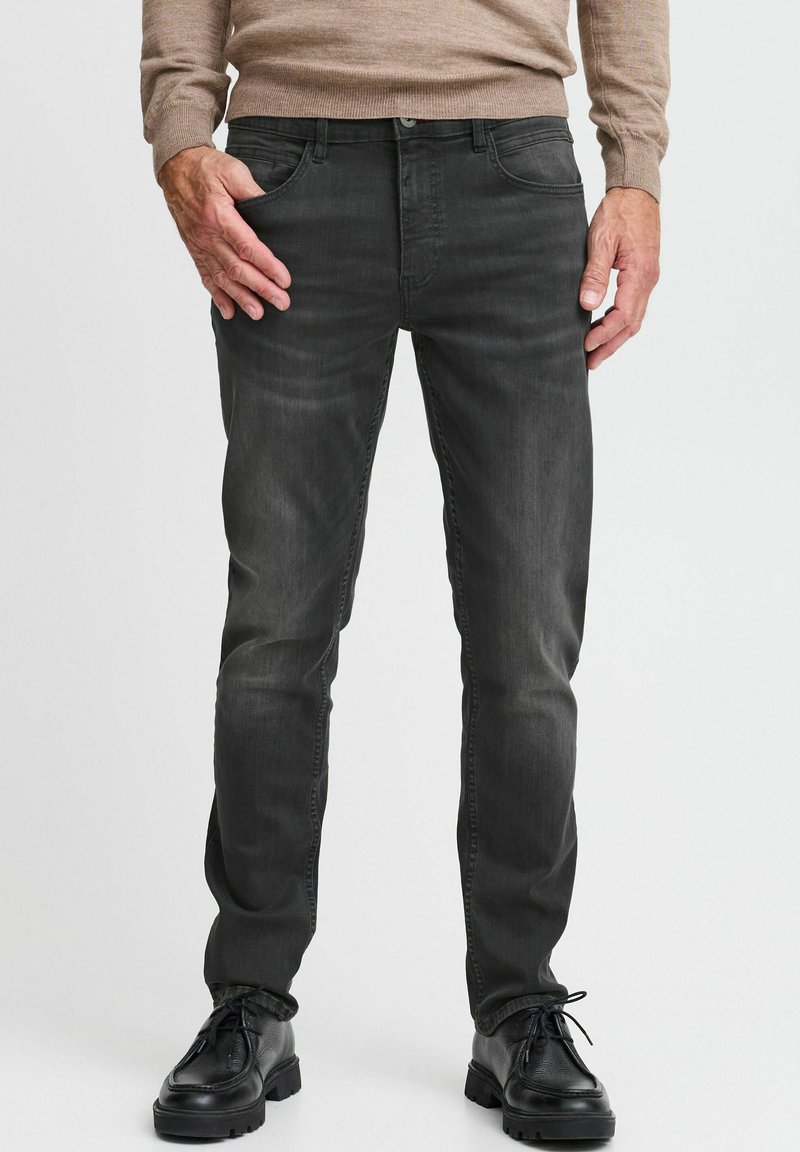 Jeans de mezclilla gris con un corte ajustado, diseño de cinco bolsillos y un ligero desgastado. Combinados con zapatos de cuero negros y un suéter beige.
