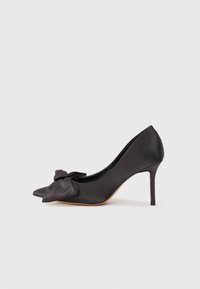 Pumps neri in satin con tacco alto, punta affilata e dettaglio a fiocco sulla parte anteriore. Presentano un tacco stiletto sottile e una texture liscia.