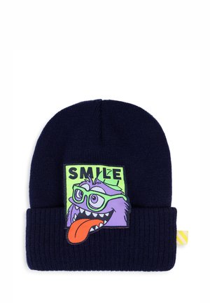 Bonnet tricoté bleu foncé avec un patch d'un monstre violet de dessin animé portant des lunettes vertes, langue tirée, et le mot "SMILE" au-dessus de sa tête.