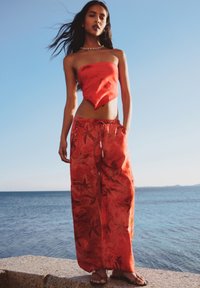 Rode strapless crop top, gecombineerd met losse rode broek met bloemenpatroon, vastgezet met een elastische tailleband; model is blote voeten.