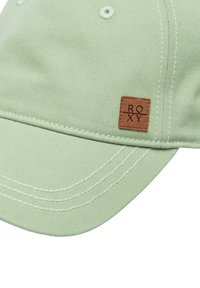 Light green baseball cap made of textured fabric, featuring white stitching and a rectangular brown leather patch with "ROXY" embossed.