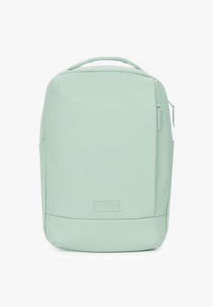 Light green backpack made of smooth, flexible material. Features a zippered front pocket, top handle, and rectangular shape.