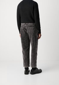 Zwarte corduroy broek met verticale strepen, met een relaxte pasvorm, twee achterzakken en gedragen met zwarte schoenen en een zwarte trui.