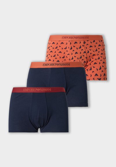 Trois boxers Emporio Armani en bleu marine et orange avec des motifs bleu marine, avec des ceintures élastiques de marque en rouge et orange.