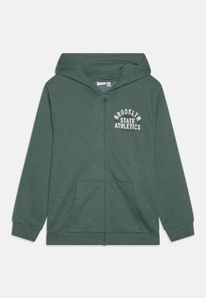 Zielona bluza z kapturem na zamek z przednimi kieszeniami i białym napisem „Brooklyn State Athletics” na lewej piersi, wyposażona w kaptur i ściągacze na mankietach.