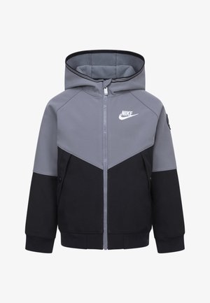 Siva in črna zip-up kapuca s kontrastnim dizajnom, ki vsebuje Nike logo, stranske žepke in elastične manšete. Mehka tkanina z kapuco.