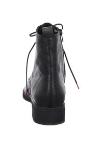 Black leather ankle boot with a smooth texture, rounded toe, and lace-up closure. Features a low heel and subtle red accent on laces.