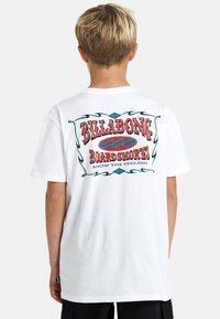 T-shirt bianco in cotone con una grafica multicolore sul retro, con la scritta "BILLABONG BOARDSHORTS" e dettagli di onde e scroll.
