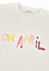 Fehér pamut pulóver, amelyen színes hímzett felirat olvasható: "OH APRIL" különböző pasztell színekben, puha tapintással.
