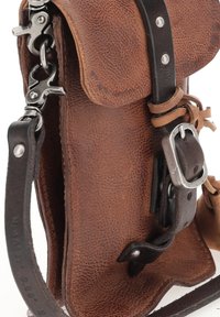 Bruine leren tas met een gestructureerd oppervlak, zilveren hardware en een afneembare schouderriem. Beschikt over een klep en een extra gespdetail.