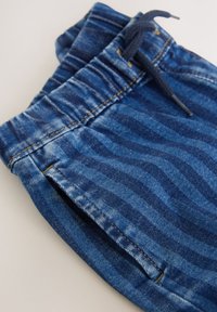 Pantaloni jogger din denim albastru cu textură în dungi, cu talie elastică și șnur ajustabil, și detaliu cu cusături galbene.